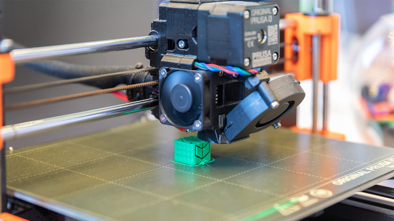 Ein 3D-Drucker druckt ein kleines, grünes, viereckiges Element.